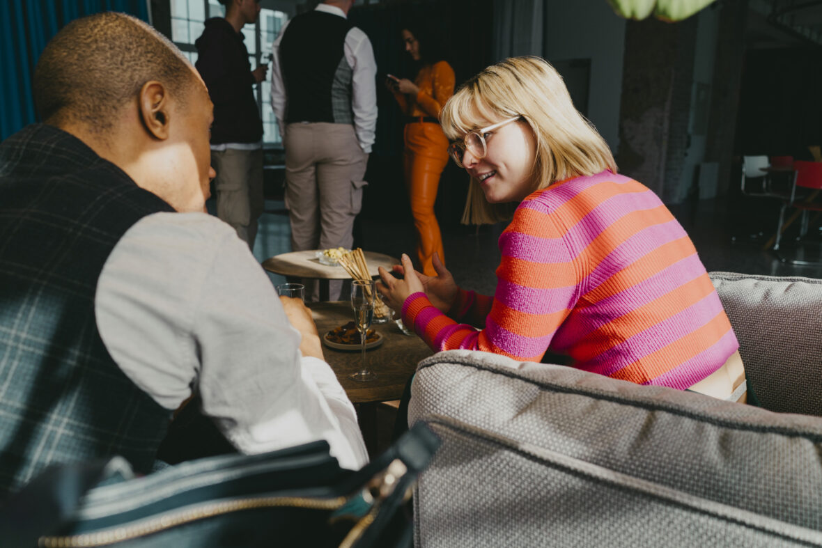 Blond affärskvinna diskuterar med kollega som sitter på soffa under evenemang.